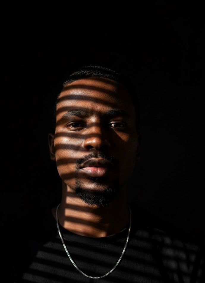 Portrait of a man with hard bands of light from a window blind falling across his face
