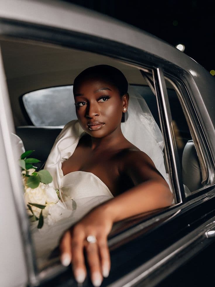 Bride holding a bouquet, framed in the open window of a vintage car